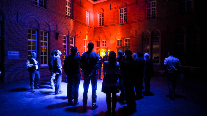Duża grupa osób rozmawia na zewnątrz pięknie oświetlonego budynku w Turnhout w Belgii podczas warsztatów zorganizowanych przez firmę Philips