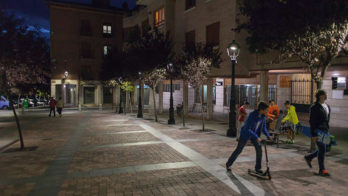 Dzieci bawią się nocą na placu w promieniach oświetlenia ulicznego Philips
