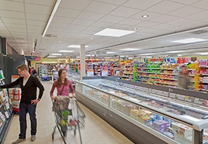 Klienci przechadzający się między alejkami supermarketu w świetle energooszczędnego oświetlenia marki Philips Lighting 