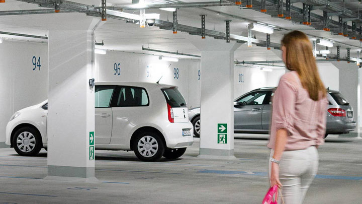 Kobieta idzie w stronę samochodu na dobrze oświetlonym podziemnym parkingu 