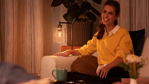 Kobieta siedząca na sofie w domu i ciesząca się przyciemnionym światłem