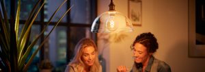 „Lampa wisząca z żarówką LED w stylu vintage oświetlająca dwie kobiety rozmawiające wieczorami, tworząc ciepłą atmosferę w miejskim mieszkaniu”.