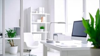 Jasne, białe pomieszczenie z biurkiem, komputerem i lampą stołową