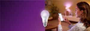 „Kobieta steruje inteligentnym oświetleniem LED za pomocą aplikacji na smartfonie, tworząc ciepłą atmosferę w przytulnym salonie dzięki technologii inteligentnego domu”.